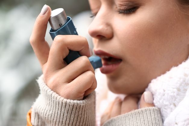 Žena drží v pravé ruce astmatický sprej při otevřených ústech.