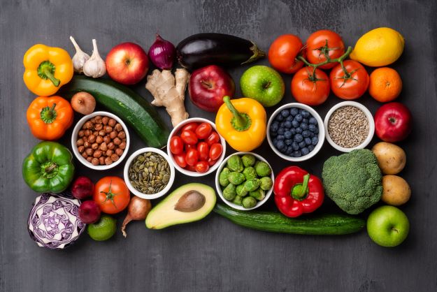 Na šedém stole jsou volně položeny zdravé potraviny, barevné ovoce a zelenina