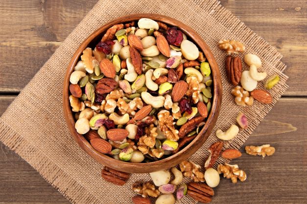 Vlašské ořechy, mandle, kešu, pekanové ořechy, pistácie jsou naservírovány v hnědé hliněné misce, která je položena na kousku jutového pytle.