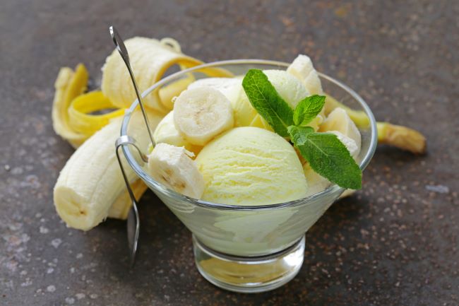 Ve skleněné sklenici jsou kopičky banánové zmrzliny s kousky čerstvého banánu, ozdobené mátou.