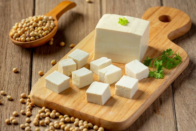tofu natural servírované na dřevěné desce s petrželkou, v pozadí je dřevěná lžíce se sójovými boby
