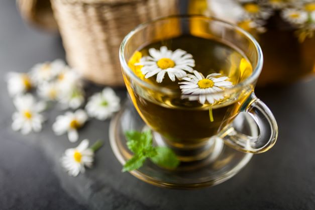 Ve skleněném šálku je heřmánkový čaj is dvěma heřmánkovými květy.