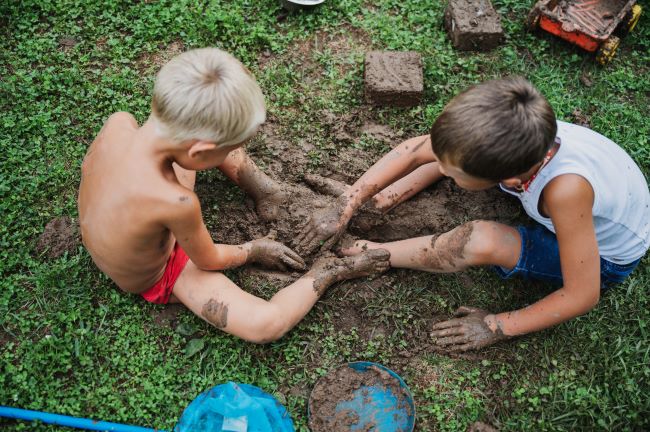 Dva kluci si v létě hrají v na zemi, jsou zabláceni od hlíny.