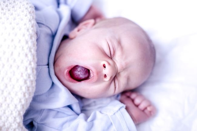 tvář novorozence zívá a na jazyku má bílý povlak. Spí v modrém oblečení